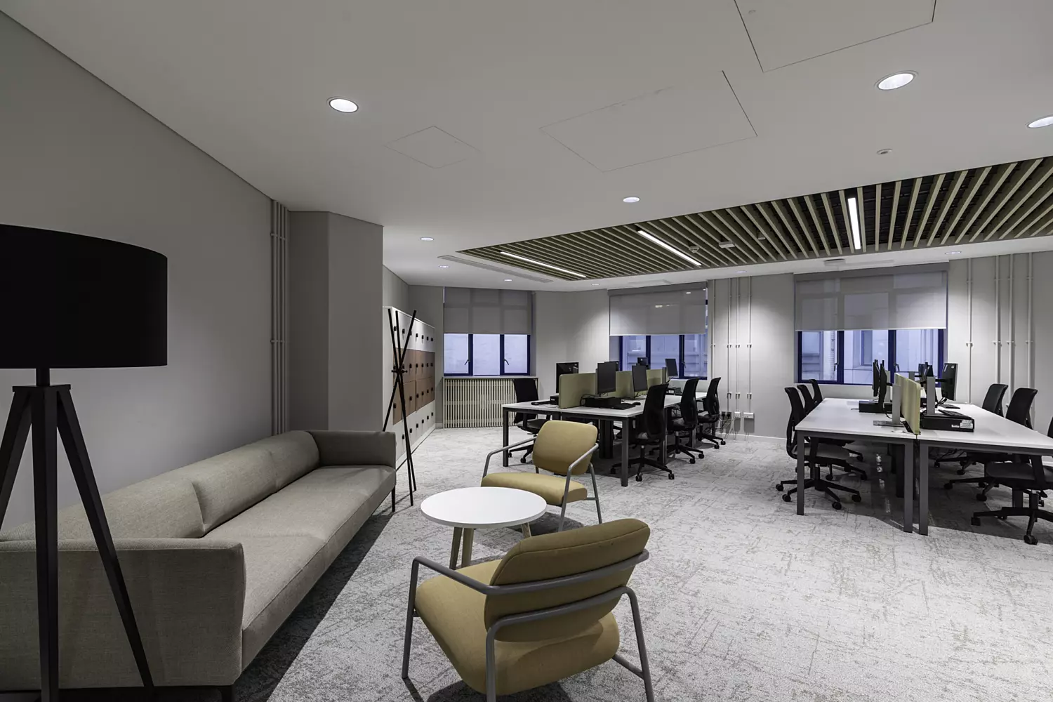 Modern office with a lounge area, workstations, wooden slatted ceiling, and large windows.