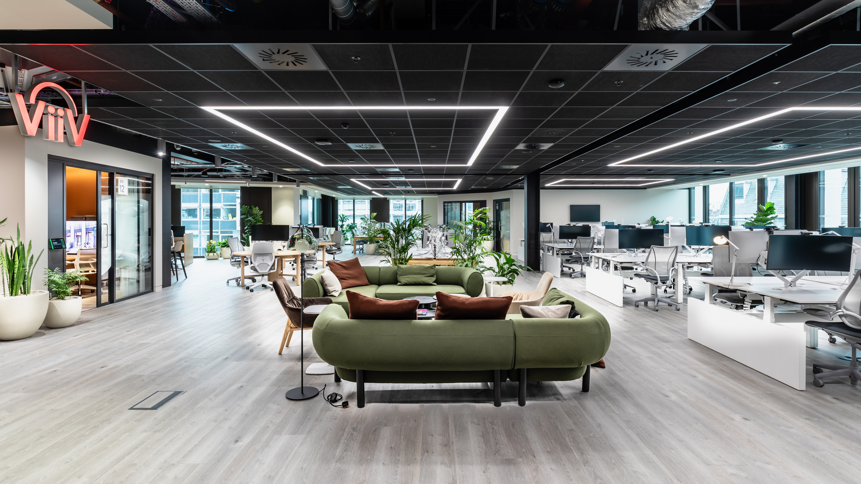 An open plan office space. Green sofas are prominent in the centre, with desks along the right and meeting pods on the left.