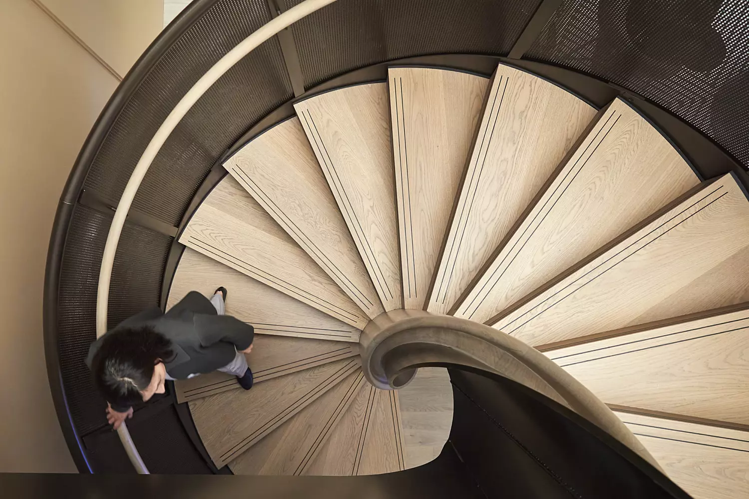 Interior view featuring a spiral staircase with wooden steps and a dark metal railing. The staircase is a central architectural element to a modern and stylish office. The design emphasises natural materials and curved forms, contributing to a contemporary and visually engaging environment.